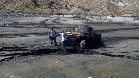 1986 Ford Bronco - A yellow off-road vehicle is stuck in thick mud with two people observing the situation.