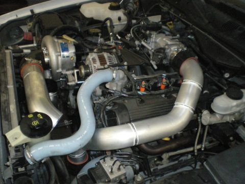 2004 Ford Crown Victoria - Aftermarket supercharger system installed in an engine bay, polished aluminum intake tubes and a silver supercharger unit.