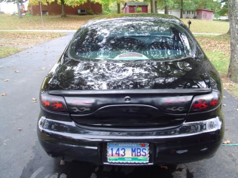 1999 Ford Taurus - Straight-on rear view of a black sedan with full-width wraparound taillights carrying red flame graphics, a lip spoiler on the decklid and…