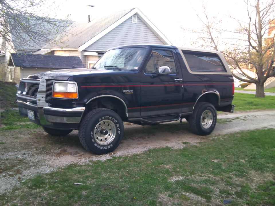 Black Ford Bronco with tan top, side view, parked on a dirt path