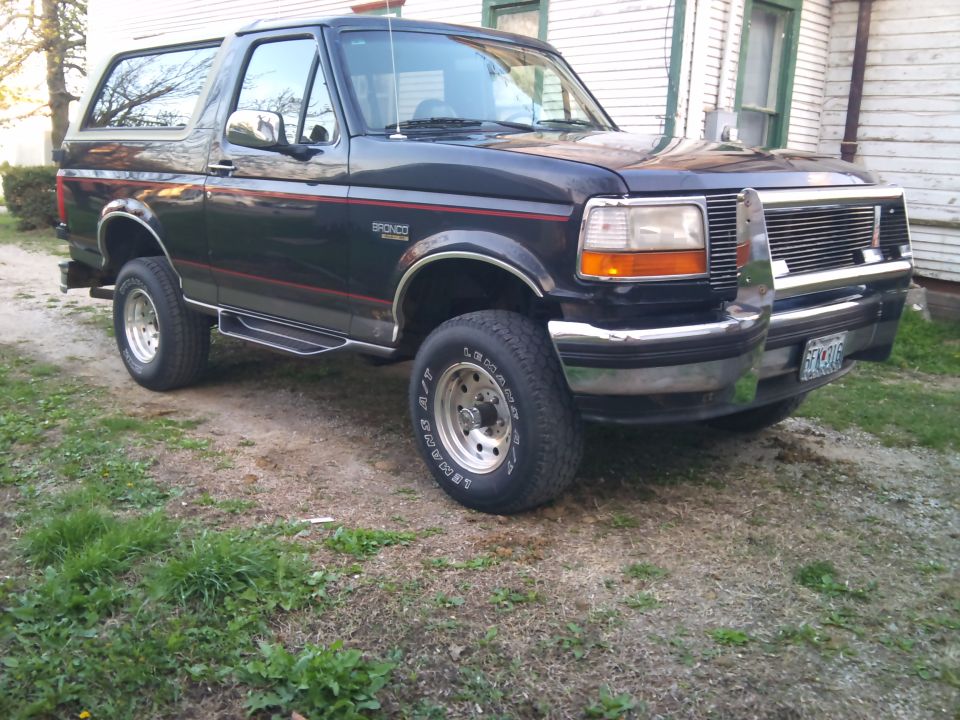 1994 Ford Bronco parked on a dirt lot next to a house