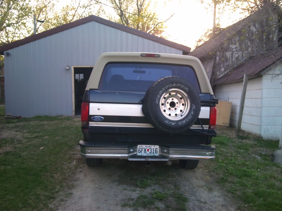 Rear view of a dark green and tan Ford Bronco with a spare tire mounted on the back. License plate reads 6FK316
