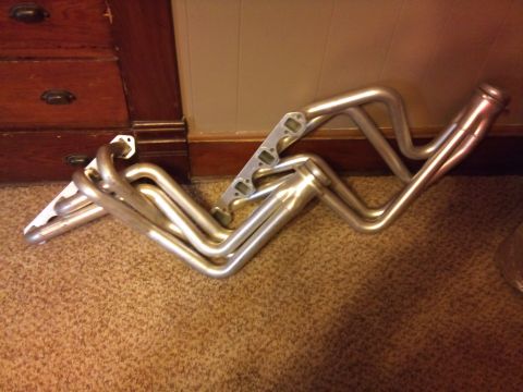 1994 Ford Bronco - Exhaust headers are shown on a carpeted floor next to wooden furniture.