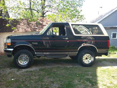 1994 Ford Bronco - Side profile of a black 1994 Ford Bronco with a white top and red pinstripes.