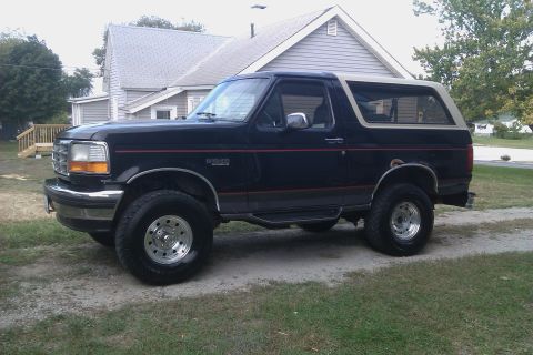 1994 Ford Bronco - This Ford Bronco is parked in front of a house with a wooden deck and trees in the background.