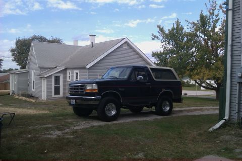 1994 Ford Bronco - A black Ford Bronco is parked in front of a house on a cloudy day.