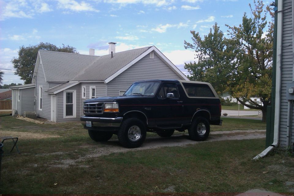 Black Ford Bronco with a tan top parked in a grassy yard next to a house