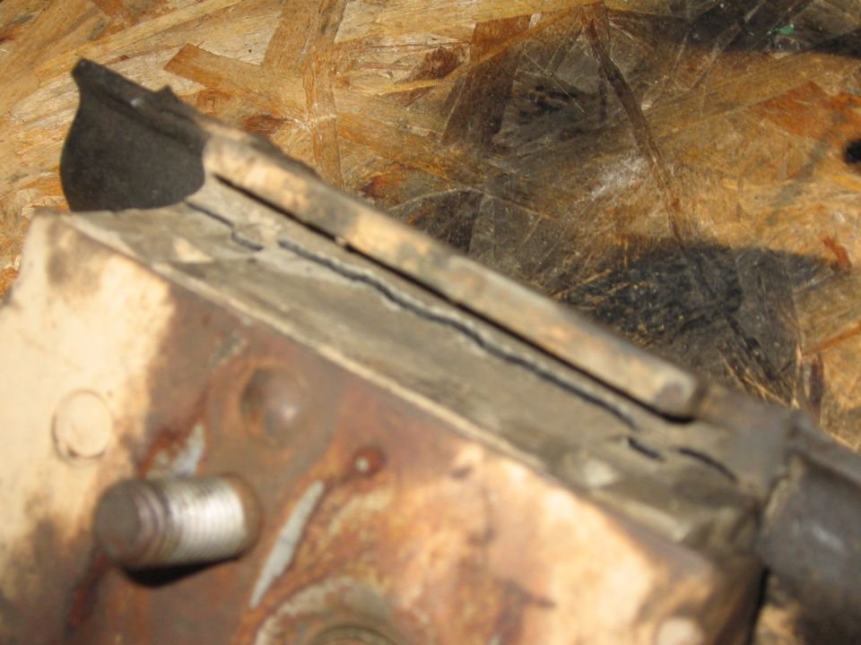 Rusty welded steel bracket with threaded stud resting on an OSB board