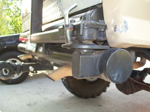 1990 Ford Bronco - The rear of a vehicle shows a trailer hitch with a spring-loaded mechanism and a metal toolbox above.