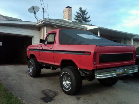 1979 Ford Bronco - Rear view of a red 1978 Ford Bronco a black soft top and lifted suspension.