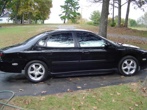 1999 Ford Taurus - Side profile of a black sedan with tinted windows and aftermarket wheels.