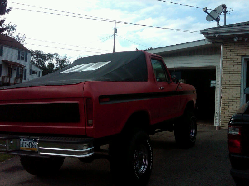 Red 1978 Ford Bronco with black soft top, rear 3/4 view, lifted suspension, chrome bumper, license plate HTX-4366