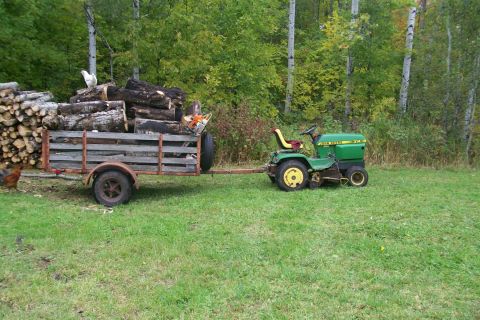 1963 Hummer H3 - A John Deere tractor tows a trailer laden with firewood through a grassy field.