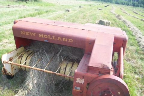 2000 Chevrolet Tahoe - A New Holland baler is shown in a grassy field, with cut hay visible within its mechanism.