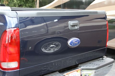 2006 Ford F-350 - The rear of a blue Ford Super Duty pickup truck is shown, reflecting another vehicle in its side panel.