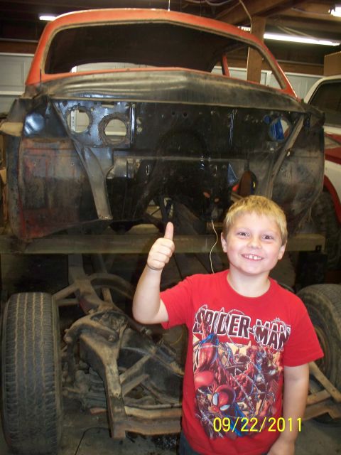 1990 Ford Bronco - A young boy poses with a vehicle undergoing restoration, showing the front end with the engine compartment exposed.