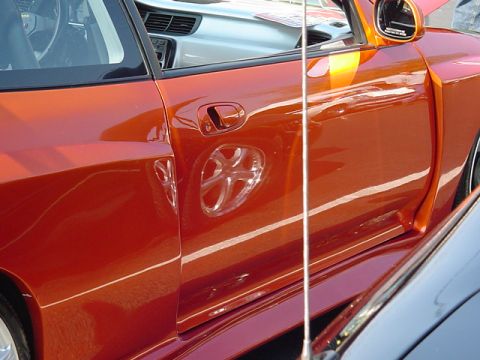 1999 Ford Taurus - A close-up of an orange car's side door reveals a custom accent within the wheel well, with another vehicle visible beside it.