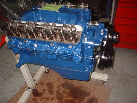 1969 Ford Mustang - A blue V8 engine is displayed on a stand, with visible internal components and drive pulleys.