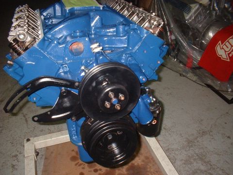 1969 Ford Mustang - A blue engine block with black pulleys and brackets is shown, mounted on a stand.