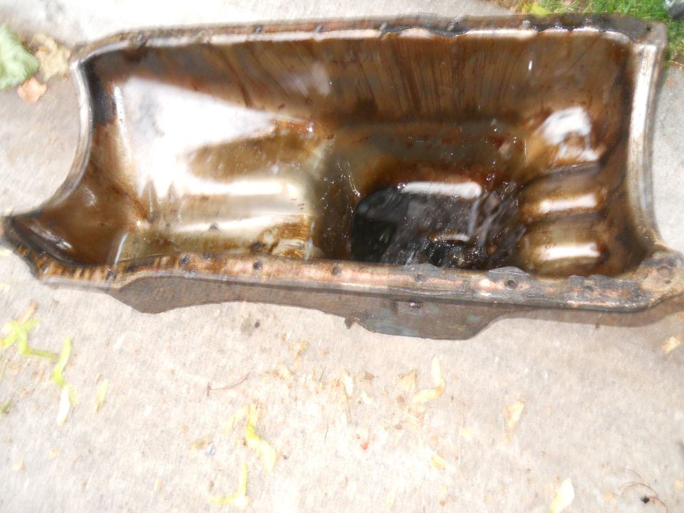 Dirty oil pan with some liquid inside, sitting on concrete
