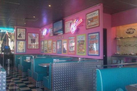 1991 Ford LTD Crown Victoria - A retro-themed diner interior features teal booths, a checkered floor, and walls adorned with vintage posters and neon lights.