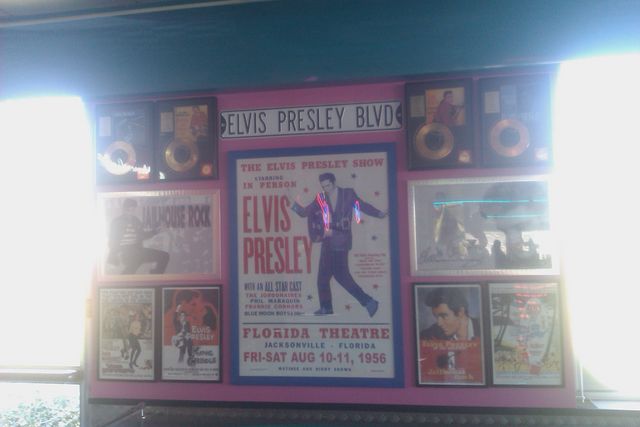 Elvis Presley memorabilia display with posters and gold records on a pink wall