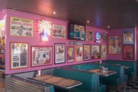 1991 Ford LTD Crown Victoria - A retro diner scene features numerous movie posters adorning the pink walls, alongside teal booths and a television.
