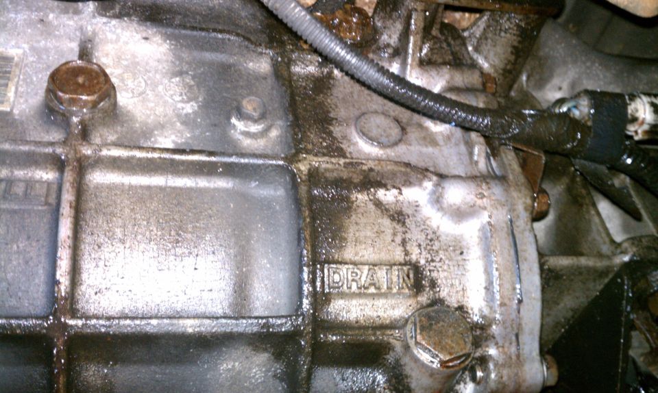 Close-up of a greasy transmission casing with the word DRAIN visible