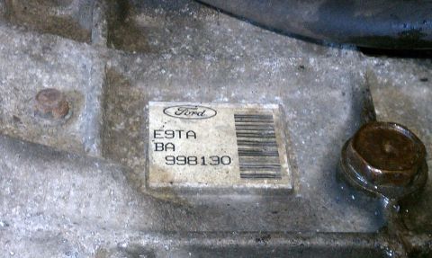 1990 Ford Bronco - A close-up view of a Ford part, possibly from a transmission, with a label containing part numbers and a barcode.