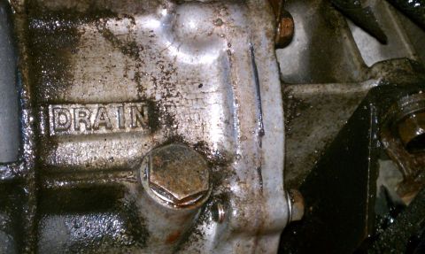 1990 Ford Bronco - A close-up view of a transmission housing shows a drain plug and the stamped word DRAIN.