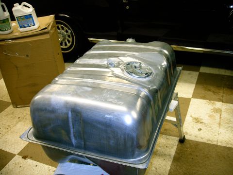 1990 Ford Bronco - A metal fuel tank is shown, with a black vehicle and a cardboard box visible behind it.