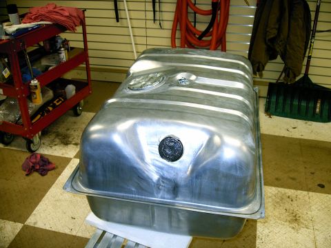 1990 Ford Bronco - A shiny metal fuel tank sits on a white surface, with a red tool cart and a rake visible in the background.