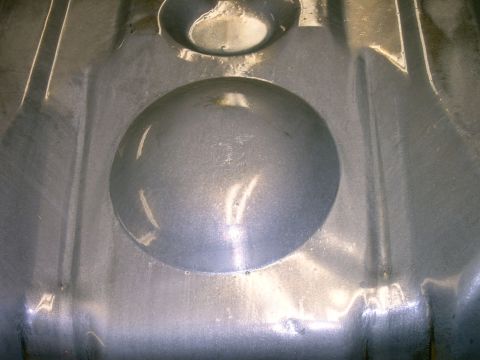 1990 Ford Bronco - Underside view of a metal fuel tank, showing its structural details and indentations.