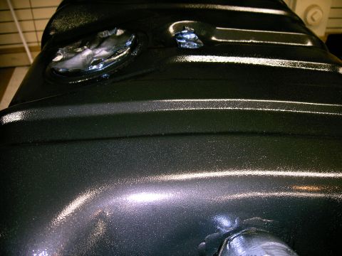 1990 Ford Bronco - A black metal fuel tank with two circular openings is shown from a close-up perspective.