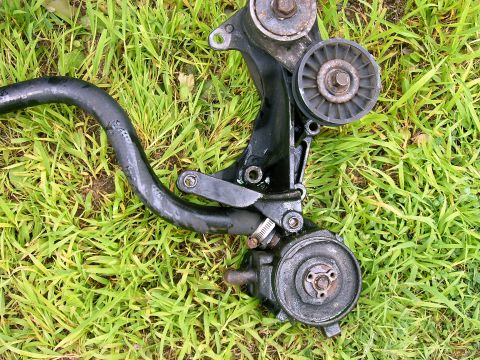 1990 Ford Bronco - Smog pump assembly with pulleys and hose, likely from an older vehicle, lying on grass.