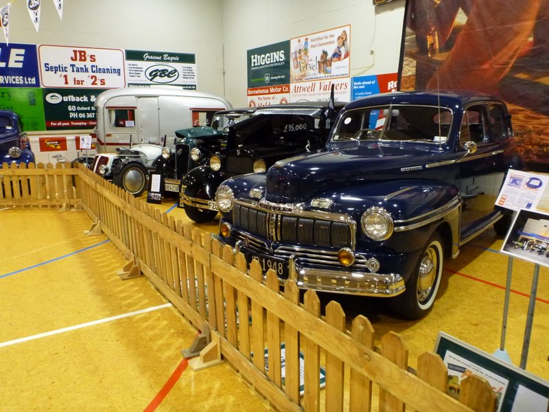 Dark blue 1948 sedan with chrome grille and headlights, parked behind a wooden fence