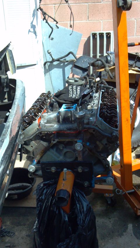 1990 Ford Bronco - Engine assembly is suspended by an orange engine hoist and resting on a stand.