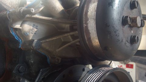 1990 Ford Bronco - Close-up of an engine water pump assembly, showing a blue gasket and a ribbed pulley.