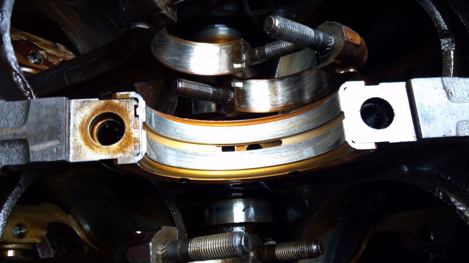 Engine crankshaft bearings with visible wear and oil residue. Part of a Supermotors.net engine rebuild
