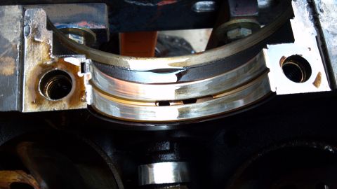 1990 Ford Bronco - Close-up of a worn engine crankshaft bearing, showing signs of damage and oil residue.