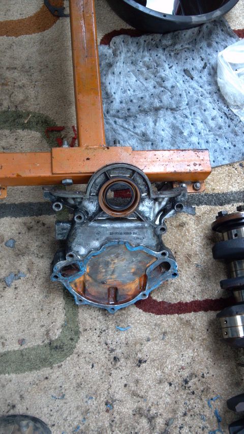 1990 Ford Bronco - Engine timing cover removed and placed on an engine stand, with a camshaft visible to the right.