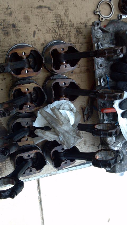 1990 Ford Bronco - Multiple engine pistons and connecting rods are disassembled and arranged on a workbench, suggesting a full engine tear-down.