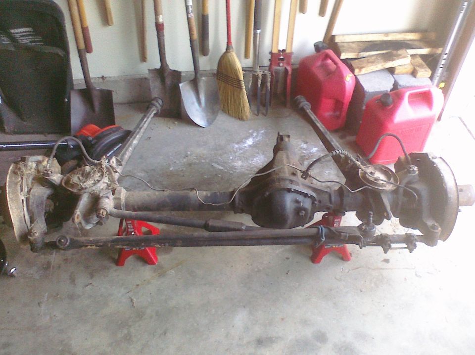 Solid front axle with differential and steering linkage on red jack stands in a garage