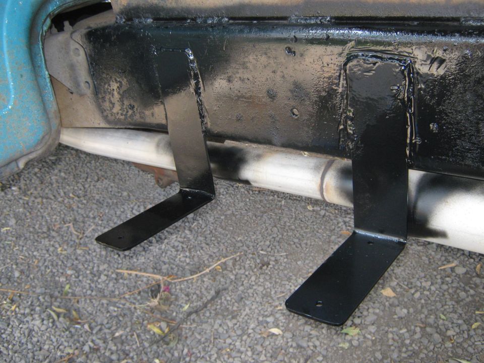 Close-up of black L-shaped brackets welded to a truck's frame rail, with exhaust pipe visible