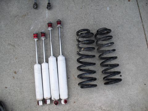 1986 Ford Bronco - Vehicle suspension parts, including shock absorbers and coil springs, are laid out on a concrete surface.