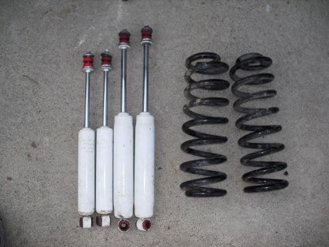 1986 Ford Bronco - A set of four white shock absorbers and two black coil springs are laid out on a concrete surface.