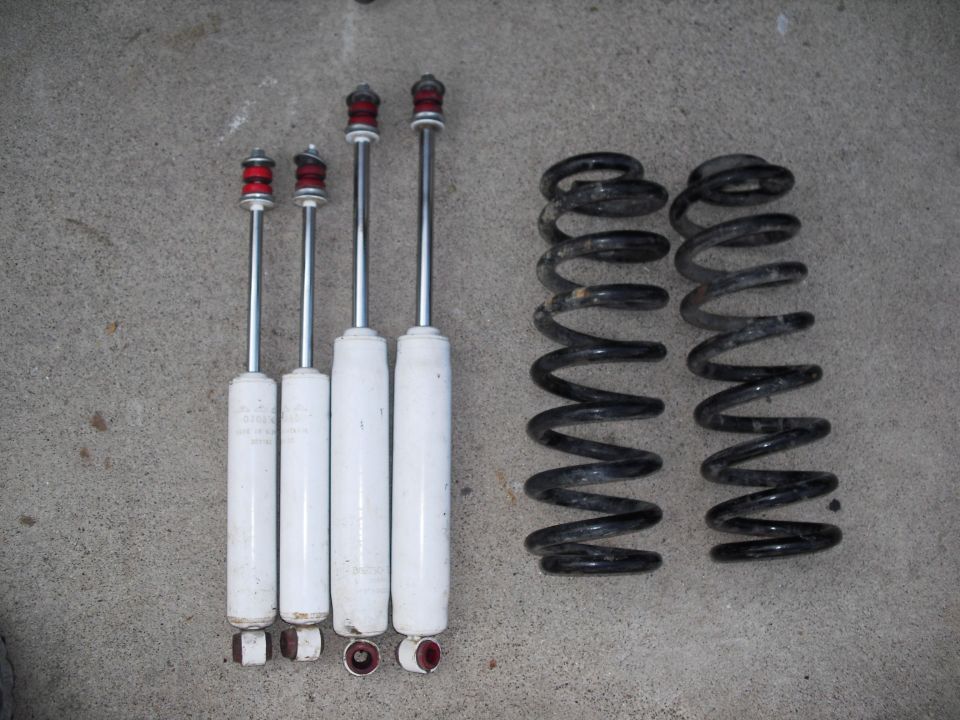 Four white shock absorbers and two black coil springs on a concrete surface