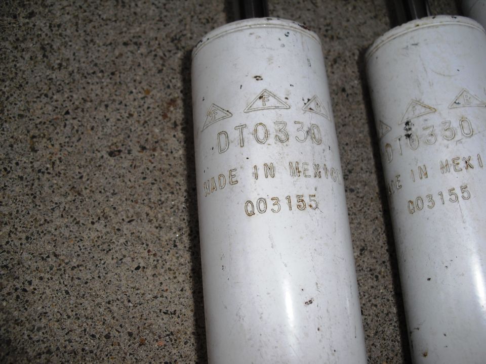 Two white shock absorbers with part number DT0330 and "MADE IN MEXICO" stamped on them