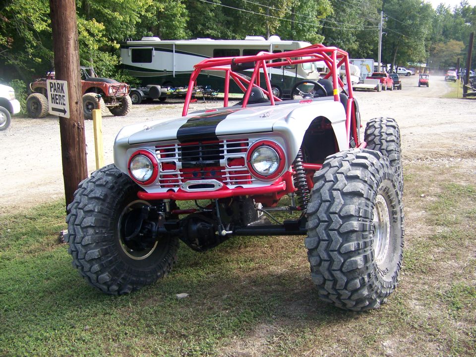 Modified off-road buggy with red roll cage and large mud tires, parked outdoors