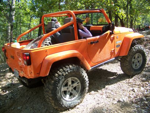2001 Dodge 1500 - An orange Jeep Wrangler navigates a wooded trail with another vehicle visible in the background.